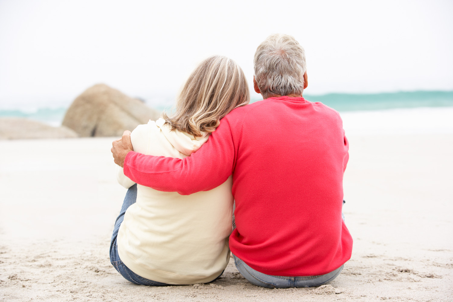 retired married couple sitting on beach looking at the ocean