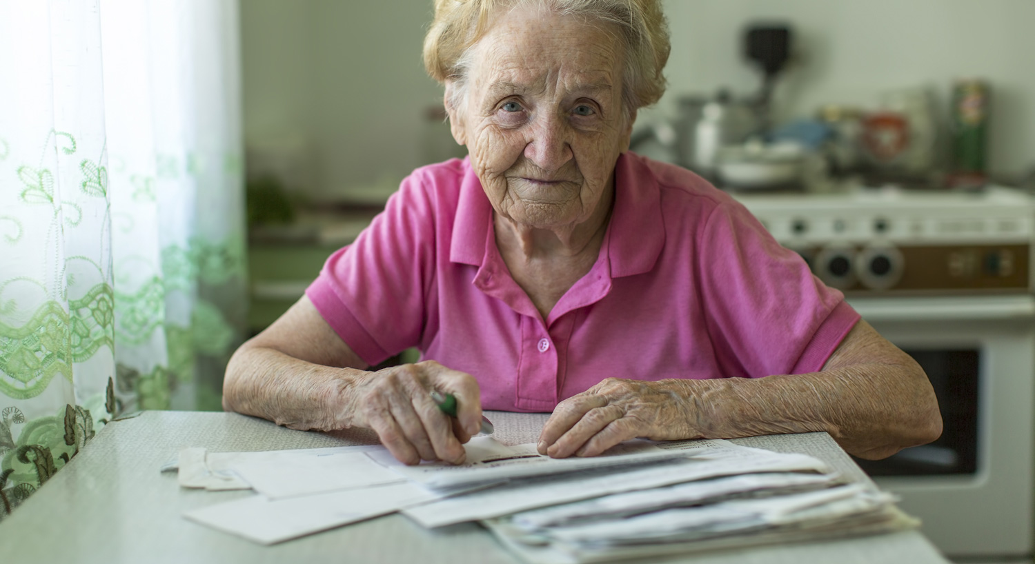 elderly woman in her kitchen doing her bills